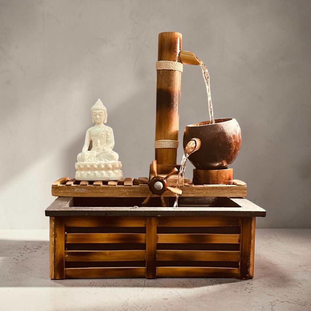 A Flow object with a bamboo, Kinetic wheel, flowing water, a wooden base, and a small white Buddha statue on a gray studio background.